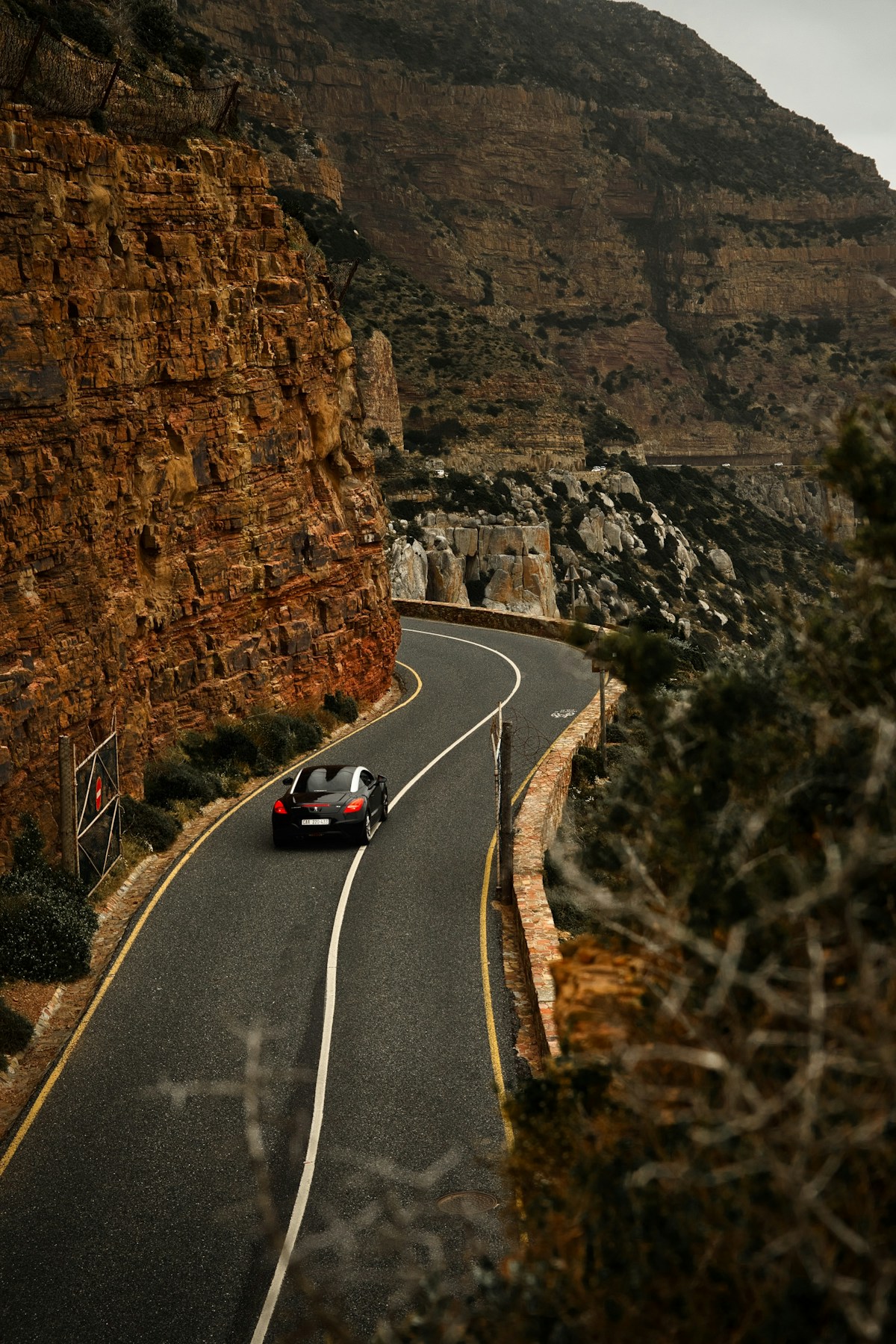 A car navigating the winding coastal road at Chapman's Peak Drive, Cape Town, South Africa