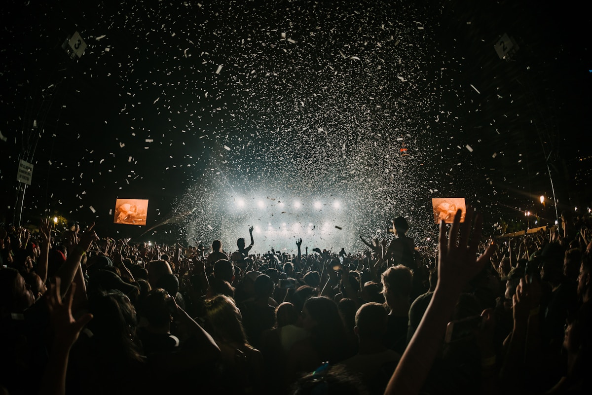 A festival crowd at night with confetti falling in front of a lit stage