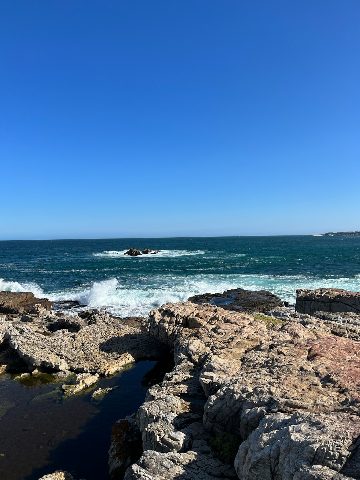Rocky coastline at Hermanus with crashing waves and blue sky, Overberg, South Africa