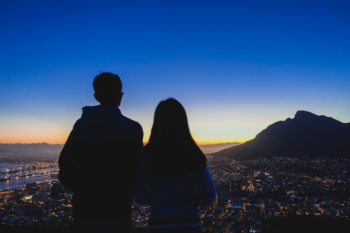Couple silhouetted against the twilight sky above Cape Town, watching the city lights from Lion's Head summit