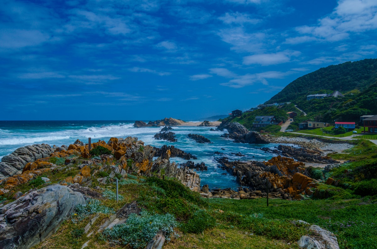 Rocky coastline with crashing waves and green hillside at Jeffreys Bay, Eastern Cape, South Africa