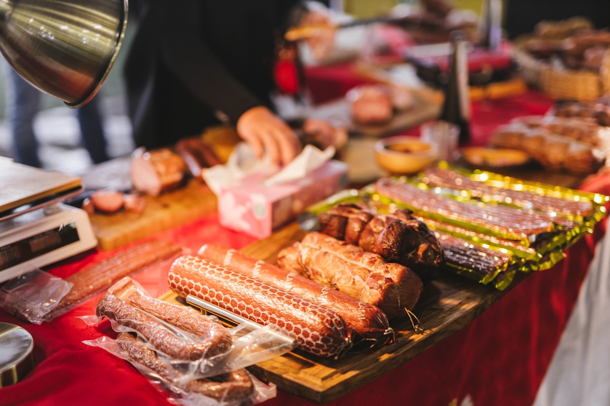 A vendor at a Johannesburg food market displaying cured meats and sausages at a wooden stall