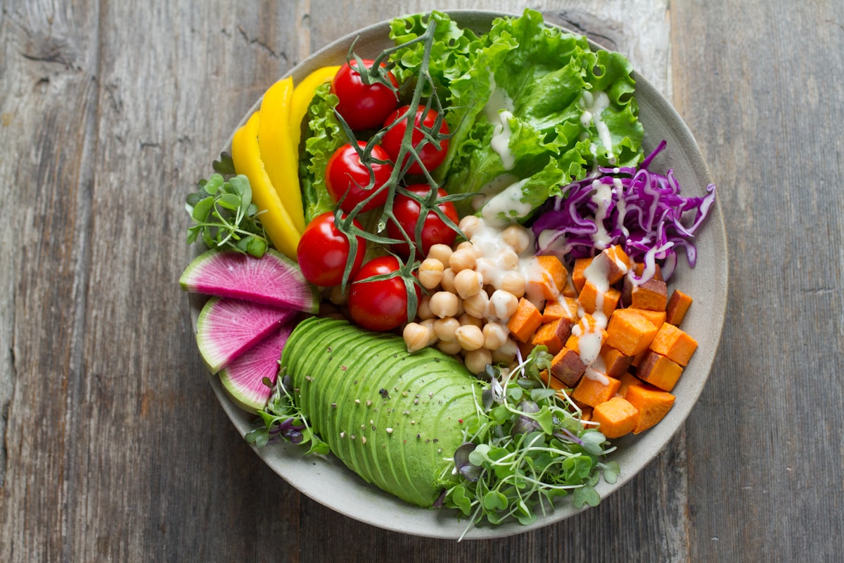Colourful vegan Buddha bowl with avocado, chickpeas, sweet potato, and fresh vegetables on a wooden table