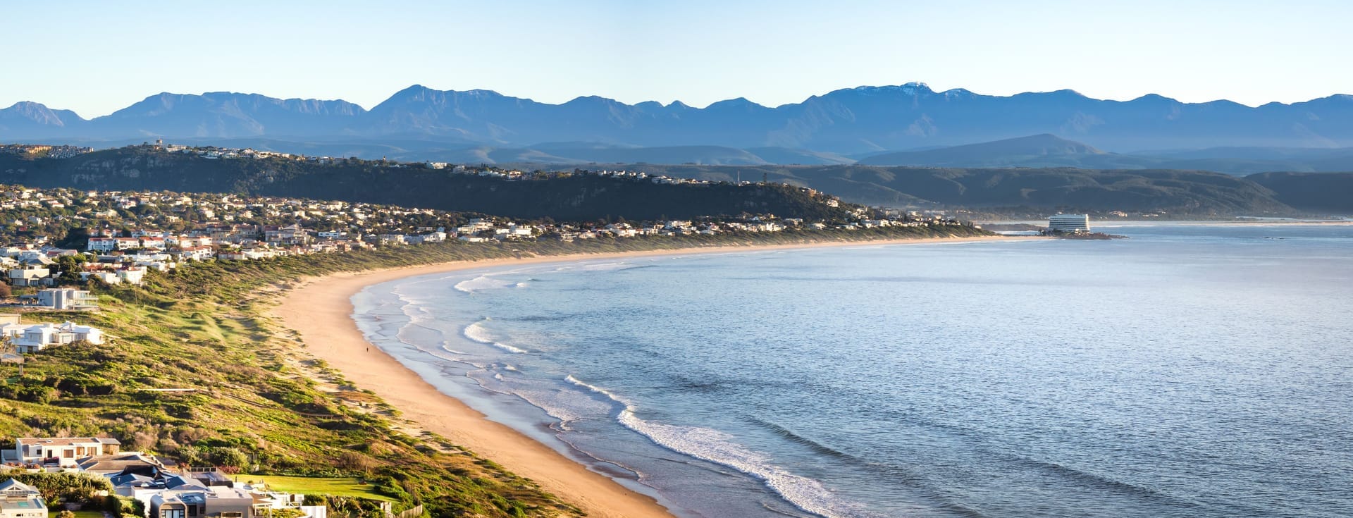 Sweeping white sandy beach at Plettenberg Bay with turquoise ocean and forested headlands, Garden Route