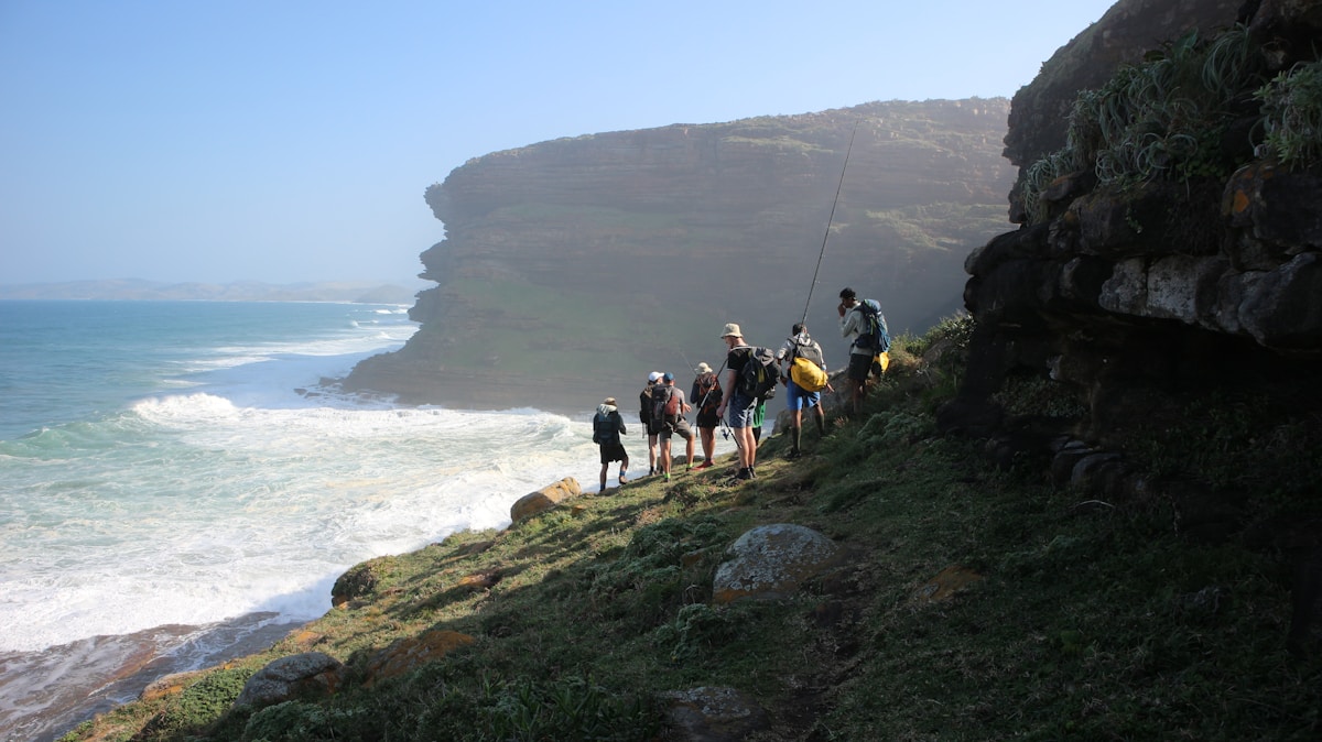 Hikers picking their way along rocky cliffs above the Wild Coast shoreline, Eastern Cape, South Africa